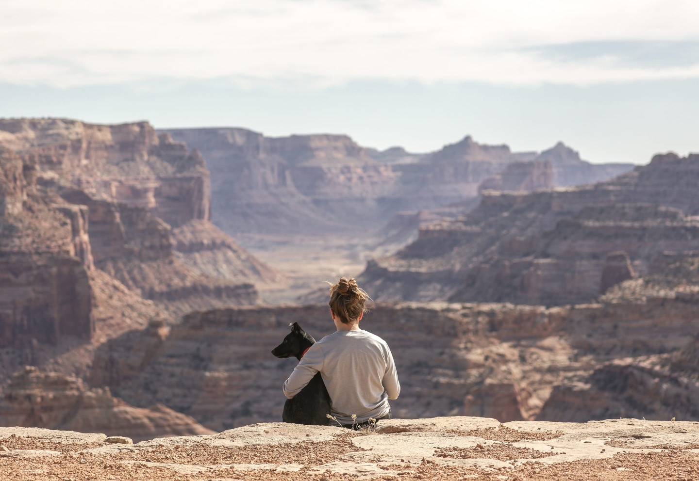 Young woman sitting on the ground with her black dog in the Grand Canyon park.