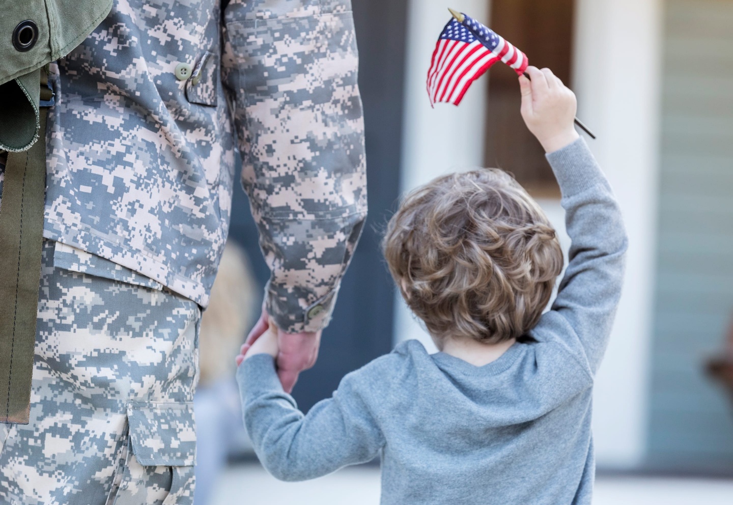 Military dressed soldier holding a young boy's hand who is holding a small American flag