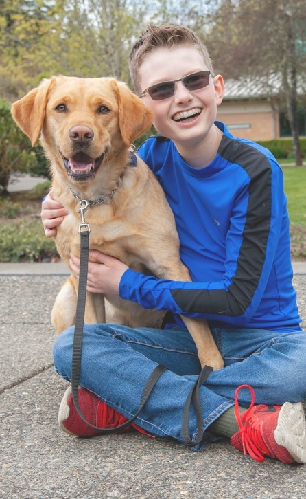 A visually impaired boy sitting on the ground hugging his golden guide dog.