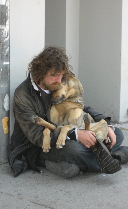 Homeless man sitting on the ground with a dog on his lap.