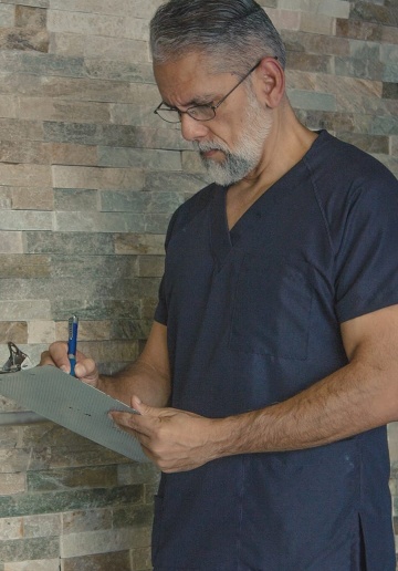 An elderly gray haired man in a bluemarine healthcare uniform filling a medical chart.