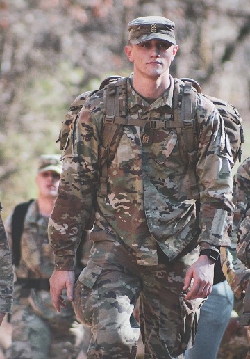Young soldier in military uniform with a backpack walking along with other soldiers.