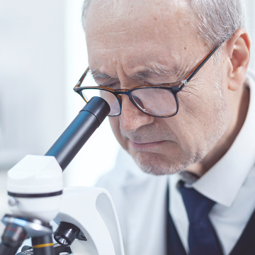 Senior scientist wearing glasses looking through the microscope.