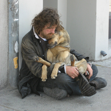 Homeless man sitting on the ground with a dog on his lap.