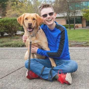 A visually impaired boy sitting on the ground hugging his golden guide dog.